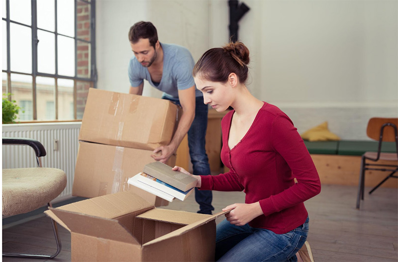Attractive-stylish-young-woman-unpacking-a-removals-carton-on-the-floor-of-their-new-home